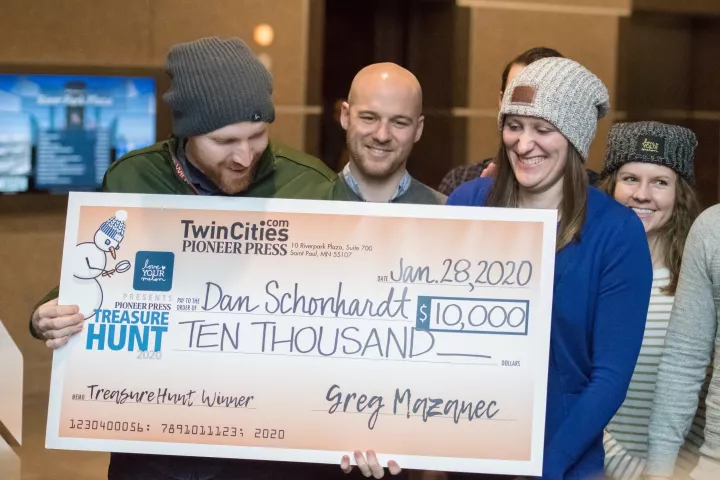 Dan Schonhardt, of Eagan, holds a check for $10,000 he received Tuesday, Jan. 28, 2020, after finding the 2020 Love Your Melon Pioneer Press Treasure Hunt Medallion with his wife, Julie. Also pictured are members of their treasure hunting team: Josh Ellingson, center, and his wife, Amy, far right. (Andy Rathbun / Pioneer Press)