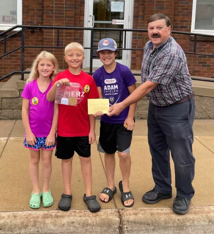 Anna, 8 and her brother, Isaac Schmidtbauer, 11, cousin Jayce Gruber, accepted the $500 in Pierz Bucks from John Kurtz of the Pierz Commercial Club.